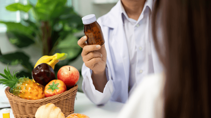 An image of a doctor holding a supplement while speaking with a patient seated in front of him.