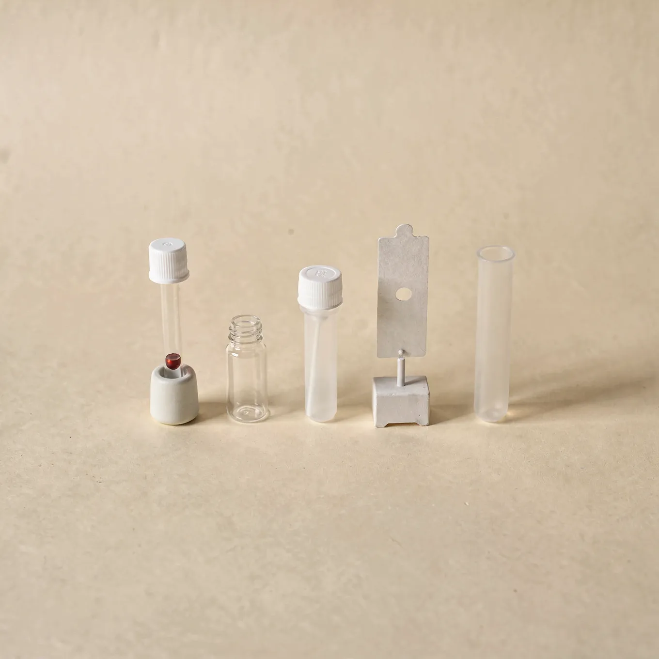 A row of five different sample collection tubes and cards on cream paper