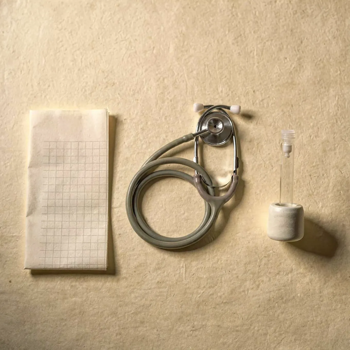 A folded grid report, a coiled stethoscope and a sample tube in a white holder, side by side on cream paper