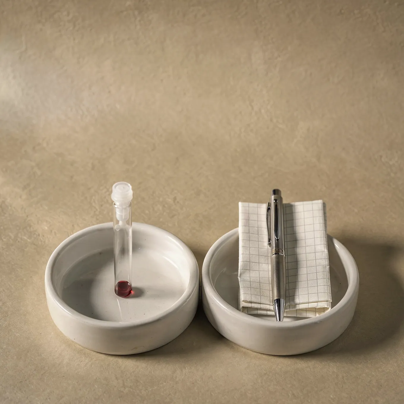 Two white ceramic dishes on cream paper, one holding a sample tube and the other a folded report