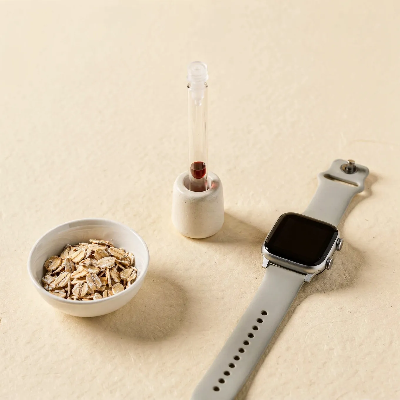 A sample tube in a white ceramic holder beside a fitness watch and a bowl of rolled oats on cream paper