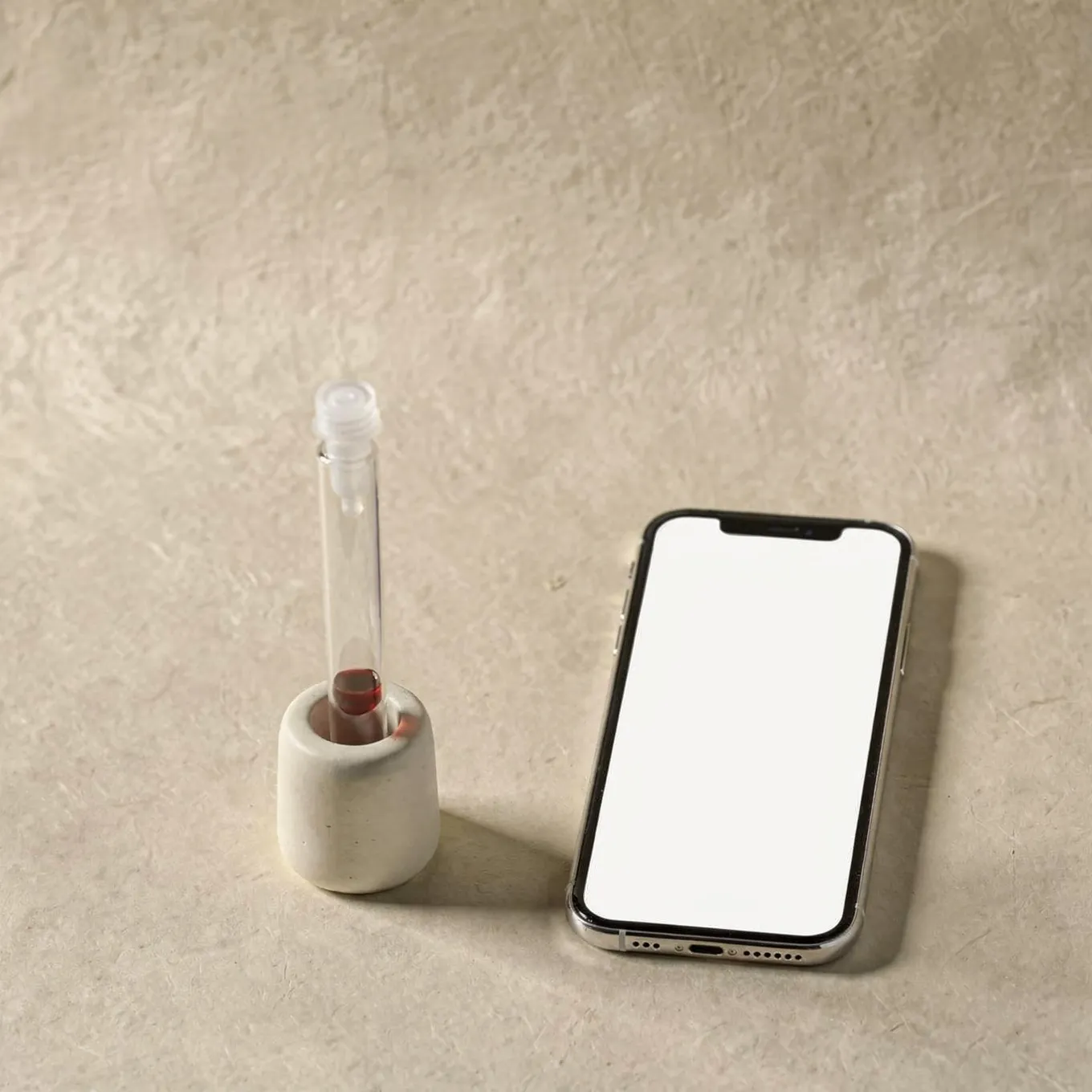 A sample tube in a white ceramic holder beside a smartphone with a blank screen on cream paper